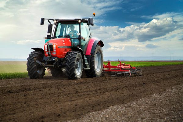 Close-up of agriculture red tractor cultivating field over blue sky